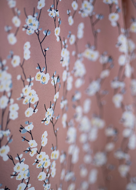 up close image of a floral pattern with white flowers, blue peals and black thin branches against a pale pink background