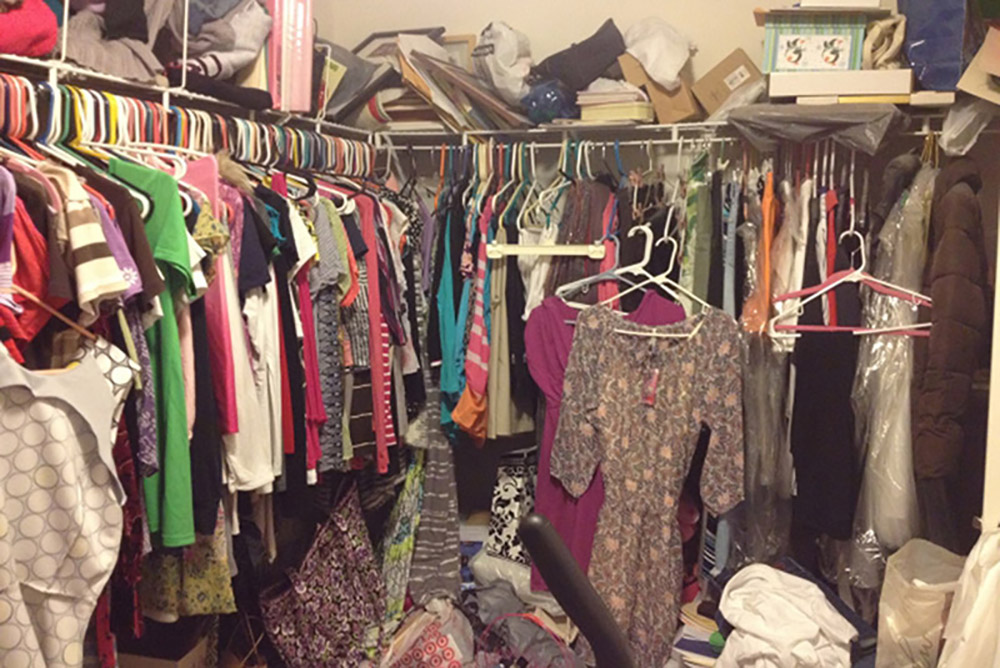 image of a messy closet featuring hundreds of hangers all displayed unorganized with mismatched shirts and dresses, and unorganized storage containers along the top