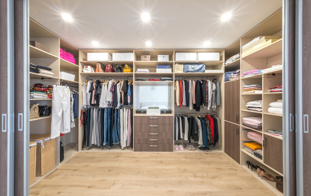 walk in closet with shelves on all sides featuring multiple racks of folded clothes, shirts and pants hanging on racks and other storage space for handbags and shoes
