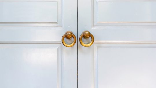 closeup of two plain white wooden doors with two small, circular brass doorknobs